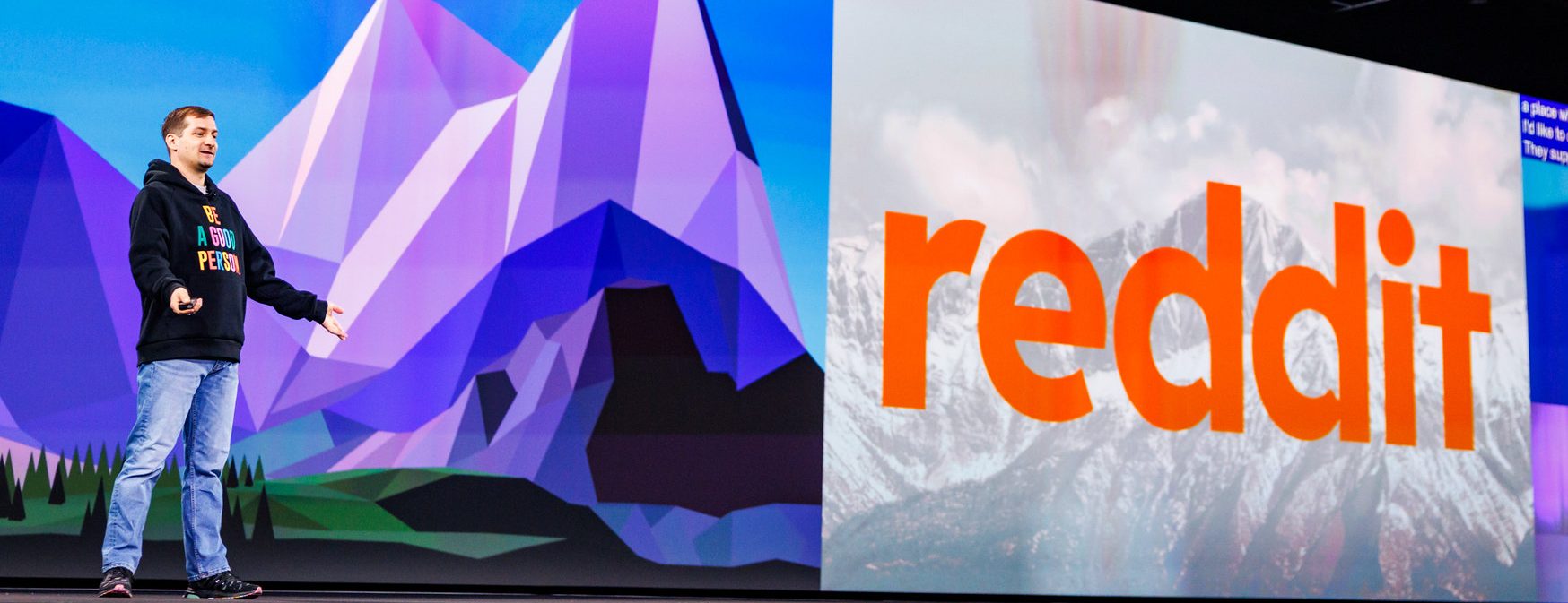 A Reddit engineer speaking on the KubeCon + CloudNativeCon keynote stage in front of a large Reddit logo